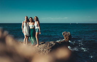 Young women standing at beach against sky