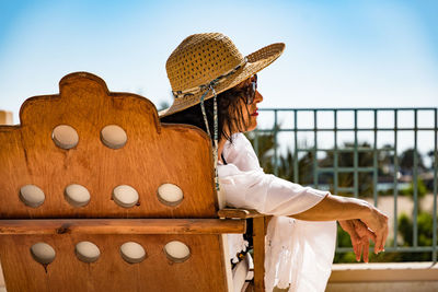 Midsection of woman sitting by railing against sky