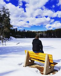 Rear view of man sitting on yellow bench amidst snow covered field