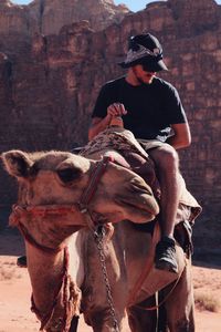 Young man riding on camel against rocky mountains