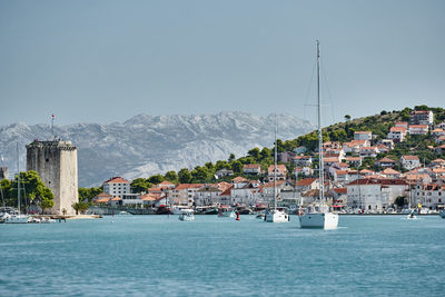 Sailboats in sea by town against sky