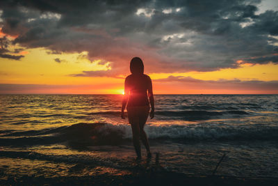 Silhouette woman standing at beach against sky during sunset