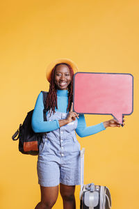 Portrait of smiling young woman using mobile phone while standing against yellow background
