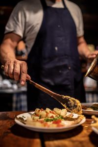 Midsection of chef serving food in plate at restaurant