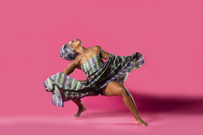 Woman in costume dancing against pink background