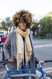 Portrait of happy woman with bicycle standing at park