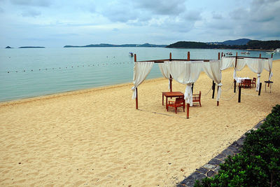 Deck chairs on beach against sky