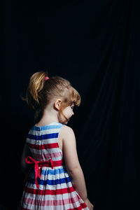 Rear view of girl standing against black backdrop