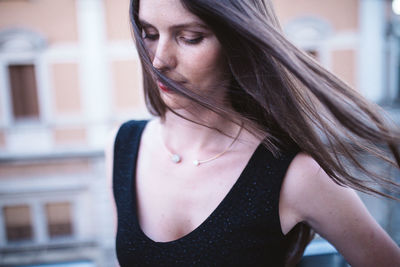 Close-up of beautiful young woman with tousled hair standing outdoors 