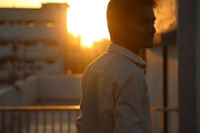 Side view of man standing against building during sunset