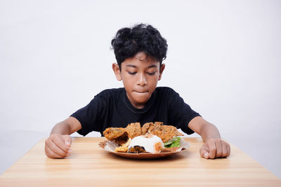 Portrait of boy eating food on table against white background