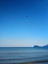 Airplane flying over sea against clear blue sky