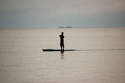 Silhouette man paddleboarding on sea during sunset