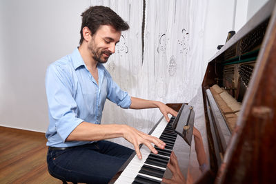 Side view of focused male musician playing piano while practicing from tablet
