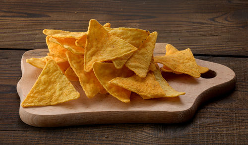 Pile of corn tortilla chips or nachos on a brown wooden background, close up