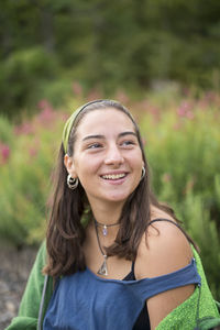 Smiling young woman looking away while standing against plants at park