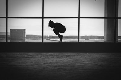 Silhouette person jumping in building against sky