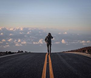 Full length of man walking on road against cloudy sky