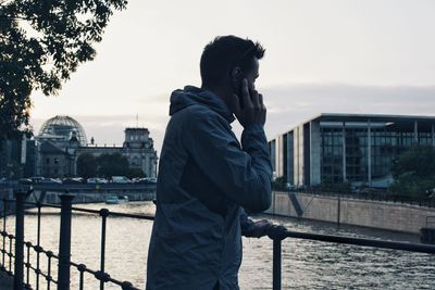 Side view of man standing by railing against river