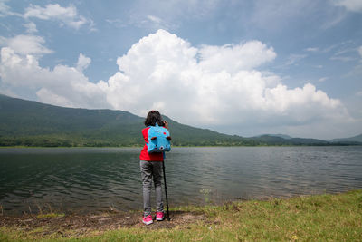 Rear view of girl standing near lake against sky