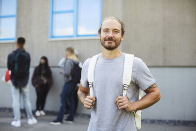 Portrait of smiling university student at campus with friends standing in background