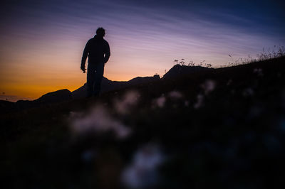 Silhouette man standing on rock against sky during sunset