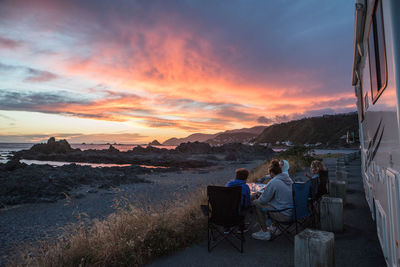 Friends on road by camper van against sky during sunset