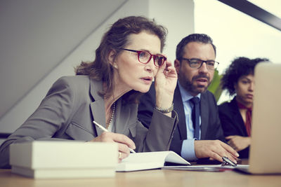 Confident senior female lawyer sitting by colleagues at office