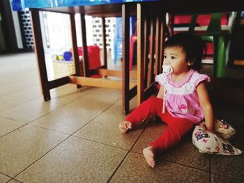 Cute boy looking away while sitting on tiled floor at home