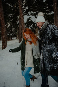 Smiling couple holding hands walking on snow covered land in forest