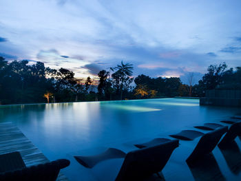 Swimming pool by lake against sky at dusk