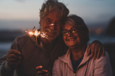 Smiling couple holding sparkler standing outdoors