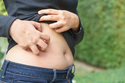 Midsection of woman scratching stomach outdoors