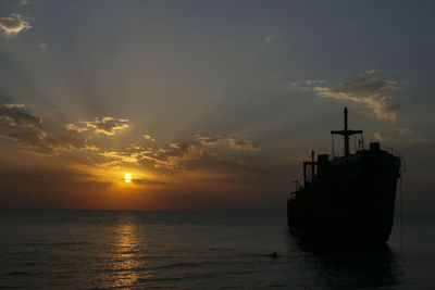 Silhouette ship moored over sea against sky during sunset