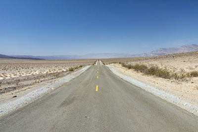 Road amidst field against clear blue sky