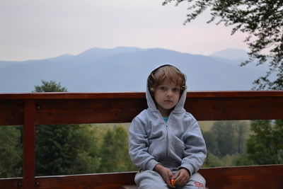 Portrait of boy sitting on bench against sky