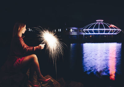 Man sitting by illuminated ferris wheel at night