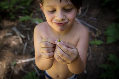 High angle view of boy looking at leaf while standing on field