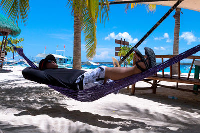 Man relaxing on hammock at beach against sky