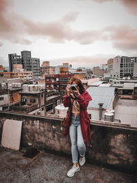 Full length of young woman standing against buildings in city