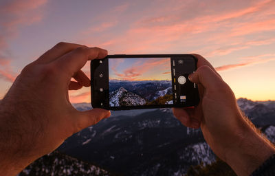 Man photographing camera on mobile phone against sunset sky