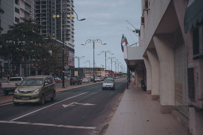 Cars on city street by buildings against sky