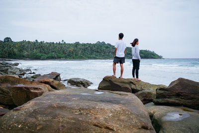 Man standing on rock looking at sea shore against sky