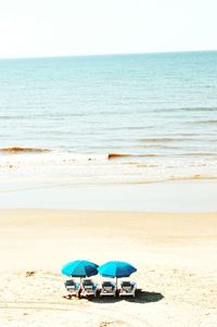 Beach chairs with umbrellas on beach against clear sky