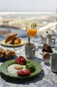 Homemade full healthy breakfast in sunlight with eggs, avocado, strawberries, blueberries, sponge cake, croissants, toast, tea, coffee and orange juice