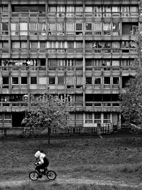 Person riding bicycle on grass field by building in city