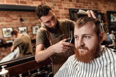 Barber cutting man's hair with hair clipper at salon