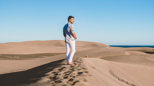 Portrait of young woman standing at desert against clear sky