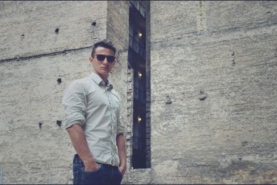 Portrait of young man wearing sunglasses standing against wall