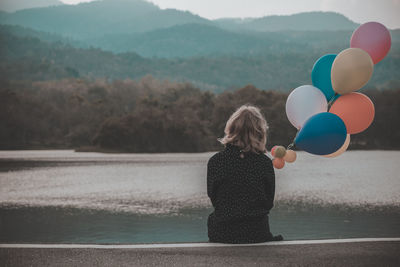 Rear view of woman with colorful balloons looking at lake during sunset